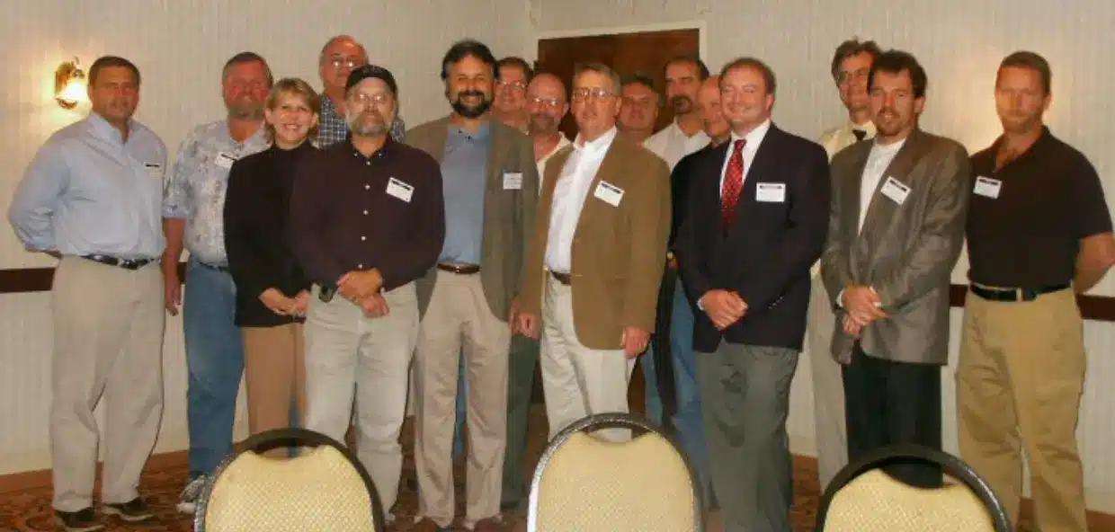 Group of people standing in a room with chairs in the foreground.