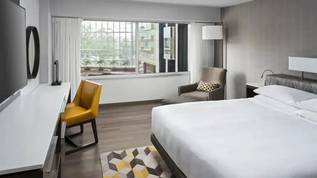 hotel information from BIMRS. Modern hotel room with a bed, desk, and large window with a city view.